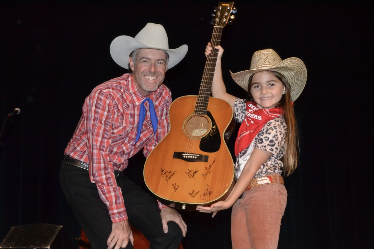 Sons of the Pioneers Trail Boss John Fullerton posing with young Kate Stewart, whose family was grateful to win this autographed guitar at the local concert two Sundays ago. Photo by Brittany Holbrooks