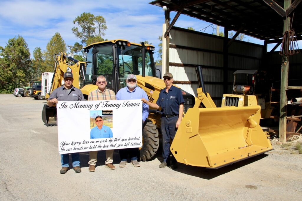 (L-R) Road Supervisor Christian Edwards, County Manager Tony Hughes, Commissioner Harold Collins and Maintenance Shop Supervisor Charles “Snuffy” Wright met last week to dedicate the new backhoe to Tommy Tanner. Photo by Shawn Jarrard